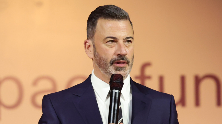 Jimmy Kimmel holding a microphone wearing a blue suit