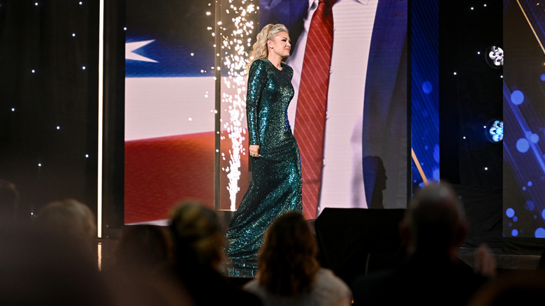 Erika Kirk walking across a stage in a sparkling, green dress
