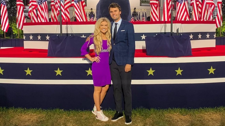 Erika and Charlie Kirk posing in front of stage dressed in U.S. flags in 2020
