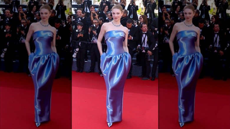 Hunter Schafer posing on a red carpet with her hands in the pockets of a shimmering blue dress