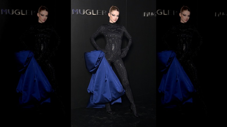 Hunter Schafer posing in a sparkling Mugler catsuit featuring a bundle of blue fabric on the hip