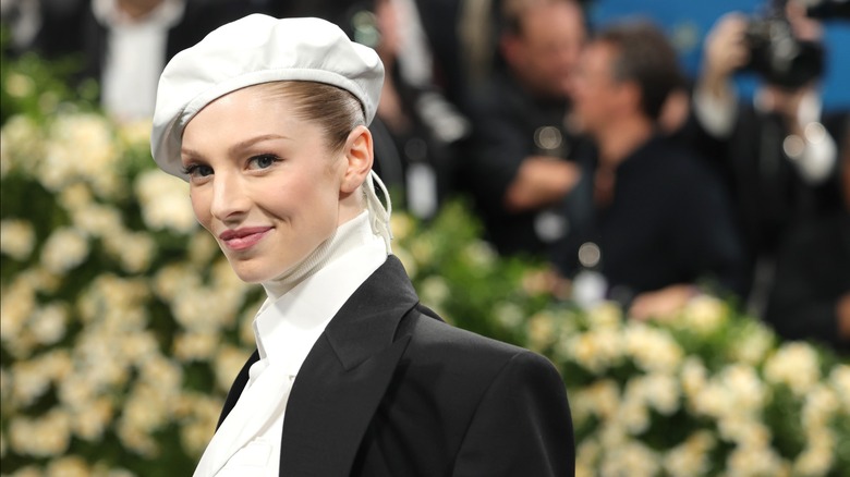 Hunter Schafer smiling at the 2025 Met Gala in a black and white suit with white hat