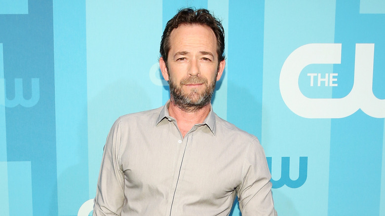 Luke Perry standing in front of a blue backdrop in 2017