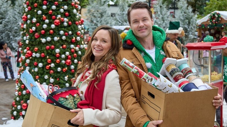 Paul Campbell and Rachel Boston smiling with boxes of wrapping paper