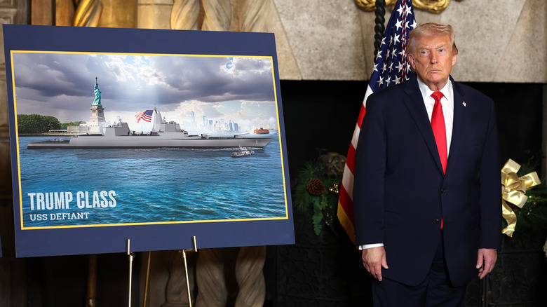 Donald Trump standing next to a drawing of the Trump class battleship USS Defiant.