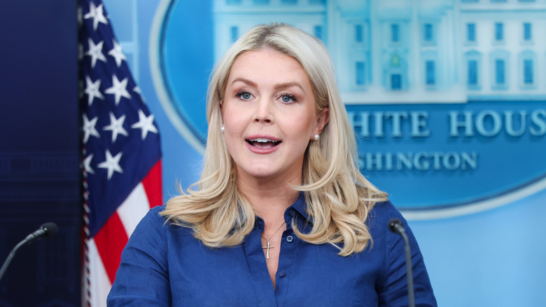Karoline Leavitt during a press conference speaking with the White House emblem and an American flag in the background.