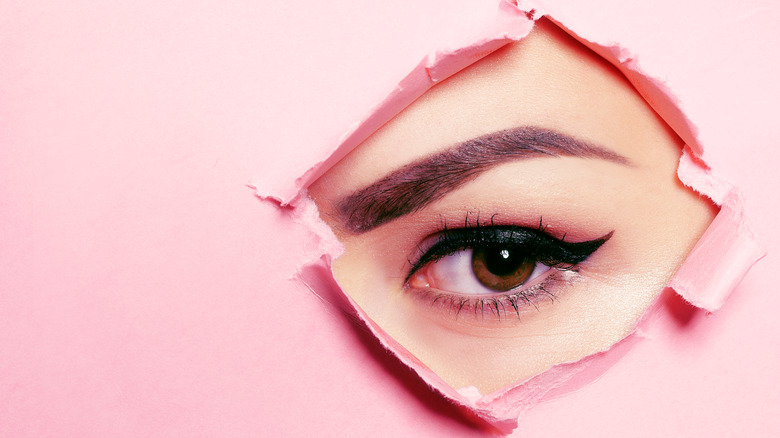 Woman's eye showing through a ripped pink paper