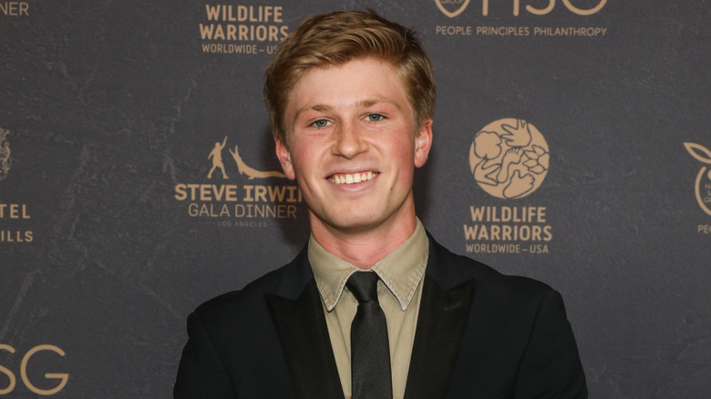 Robert Irwin smiling in a black suit with a green shirt underneath