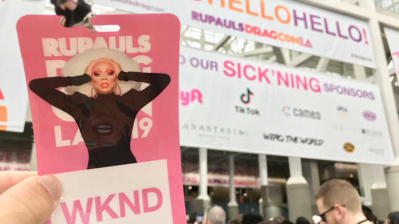 RuPaul's DragCon pass being held in front of DragCon sign