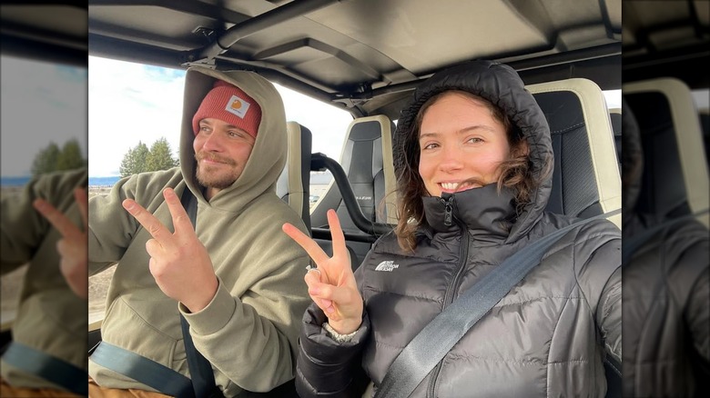 Bianca Grimes and Luke Grimes holding up the peace sign while driving in a car