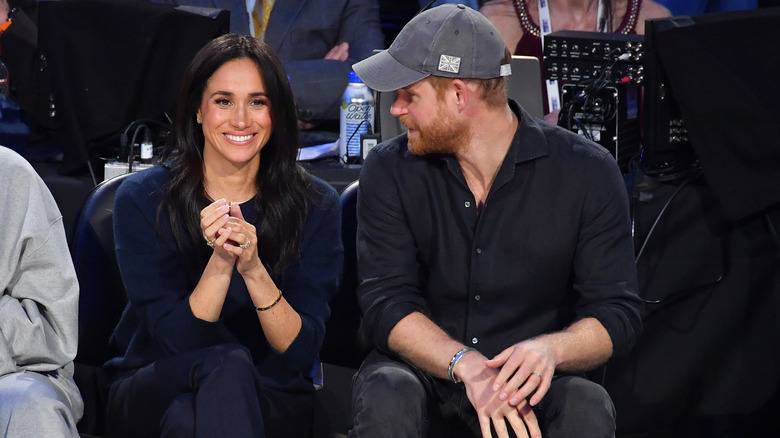 Prince Harry looking at a smiling Meghan Markle as they sit courtside