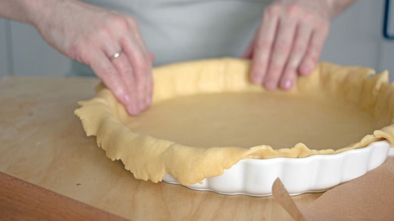 woman placing pie dough into a dish 