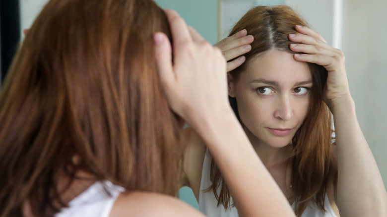 Woman looking in a mirror examining gray hair in her roots.