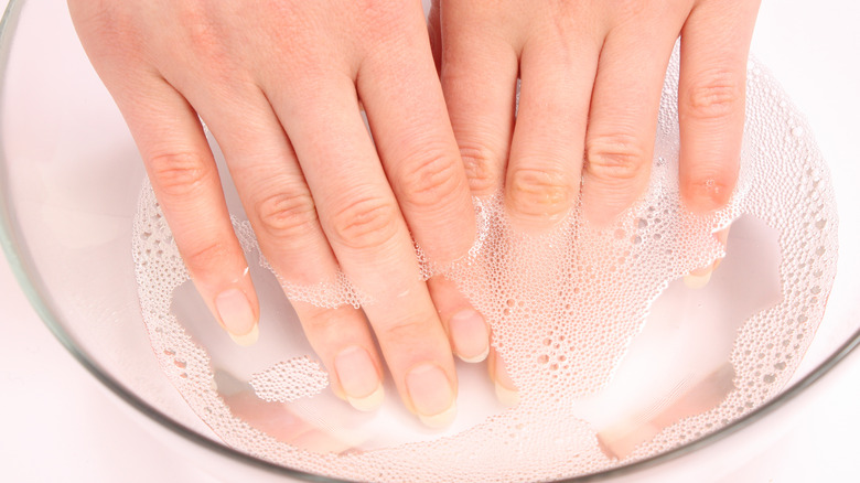 Close up of a woman's hands soaking in a clear bowl of soapy water. 