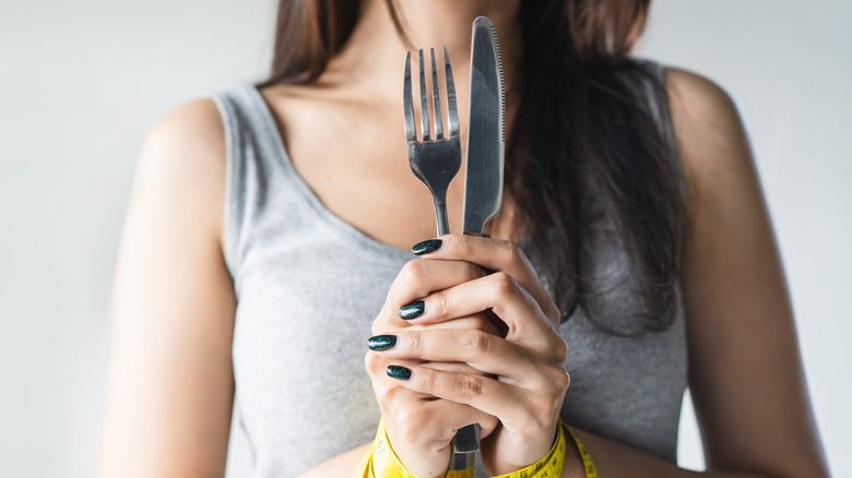 Woman holding a knife and fork with her hands tied with measuring tape