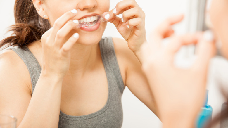 Woman applying teeth whitening strip 