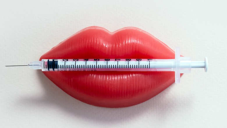 Fake red lips holding a syringe of lip filler