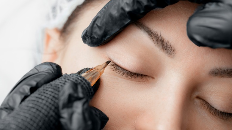 Permanent makeup artist applies tattoo to lash line