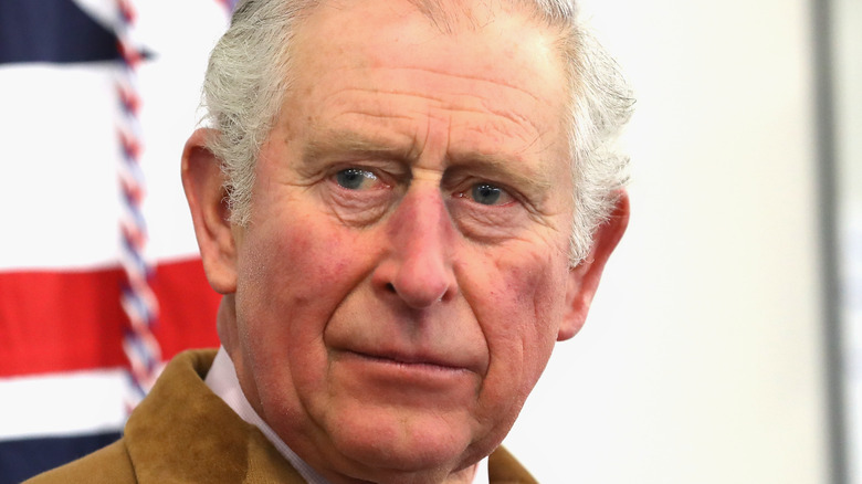 King Charles III looks serious, British flag behind him