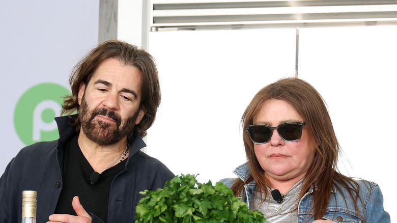 Rachael Ray in a jean jacket, silver shirt and sunglasses sitting next to John Cusimano who's wearing a black shirt and jacket at the Grand Tasting Village.