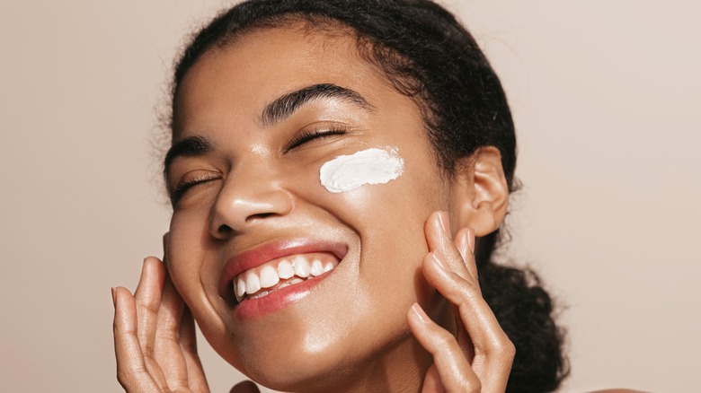 Woman smiling with stripe of moisturizer on face 