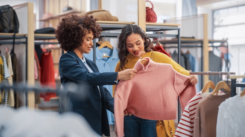 Sales associate helps woman find a sweater in store