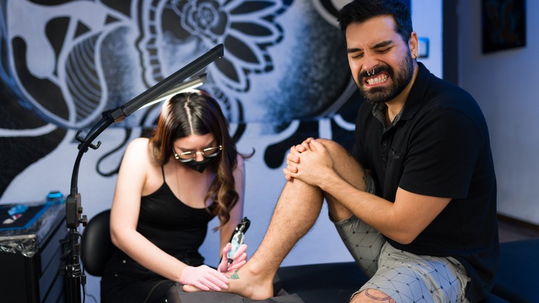 Man in pain getting tattooed on his foot