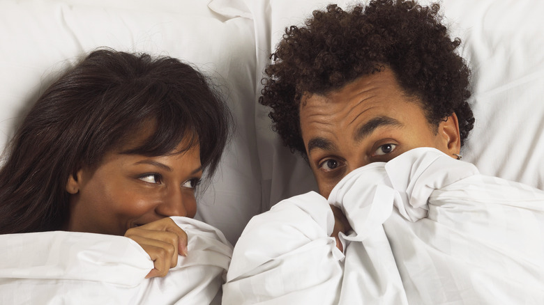 Couple peeking out from sheets