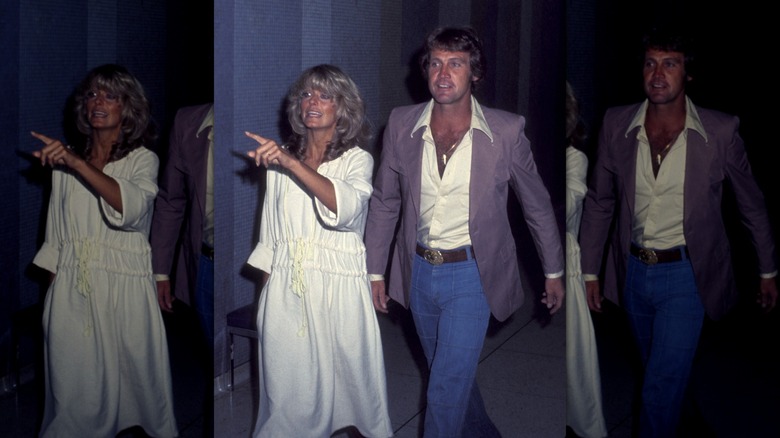 Farrah Fawcett in a flowy cotton dress pointing ahead while Lee Majors follows behind her in a gray blazer and high waisted jeans