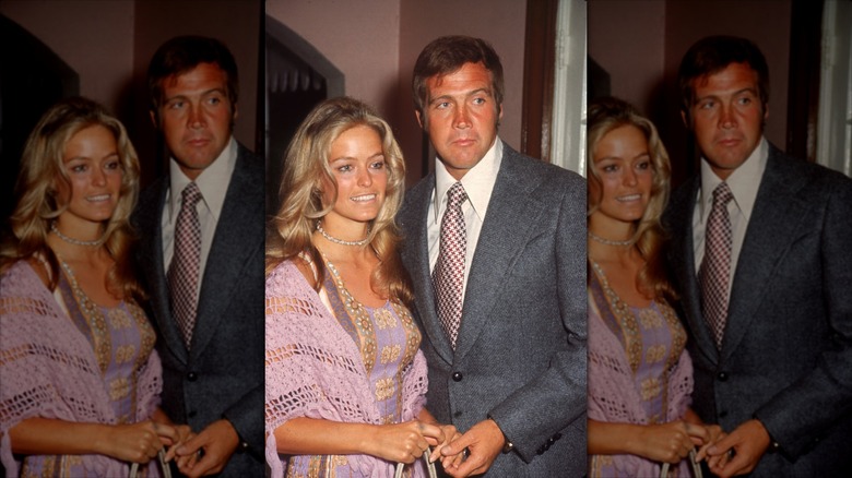 Farrah Fawcett in a lavender patterned dress and matching crochet shawl holding Lee Majors' hand as he's in a grey suit with a red houndstooth tie