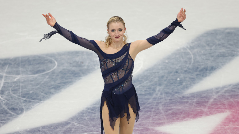 Amber Glenn on the ice with arms outstretched in navy blue skating dress with sheer panels