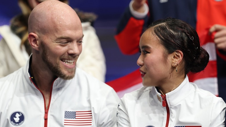 Ellie Kam and Danny O'Shea looking at each other wearing white Olympic jackets