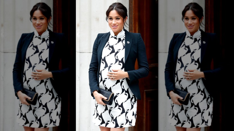 Meghan Markle wearing a black and white print mini dress and a black blazer while holding her baby bump.