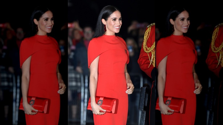 Smiling Meghan Markle wearing red dress with a matching clutch at the Mountbatten Music Festival in 2020.