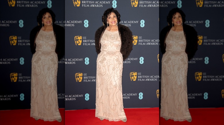 Shirley Bassey wearing a champagne colored dress with a floral embellishment and fur coat at BAFTAs dinner