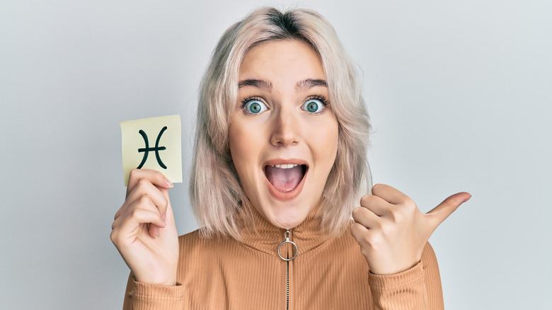 A woman holding a card with a Pisces symbol on it.