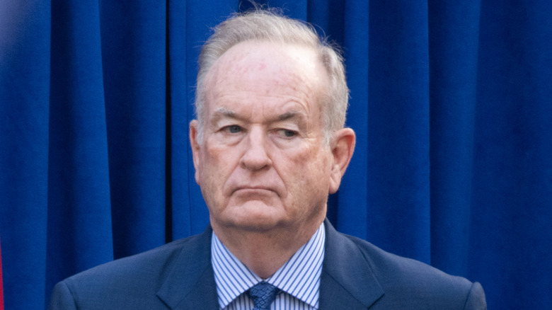 Bill O'Reilly standing against blue and red flags