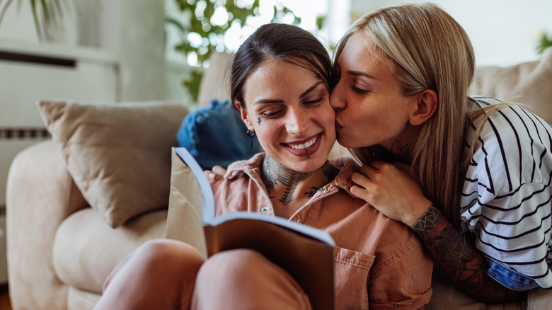 Woman reading book as girlfriend kisses her cheek