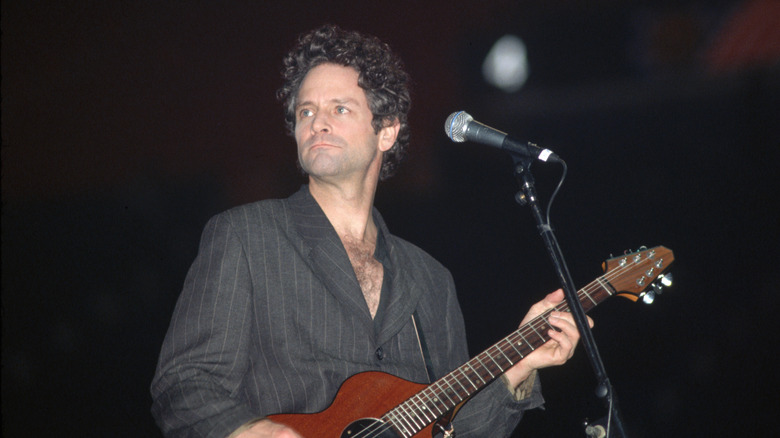 Lindsey Buckingham playing guitar onstage in a baggy blazer.