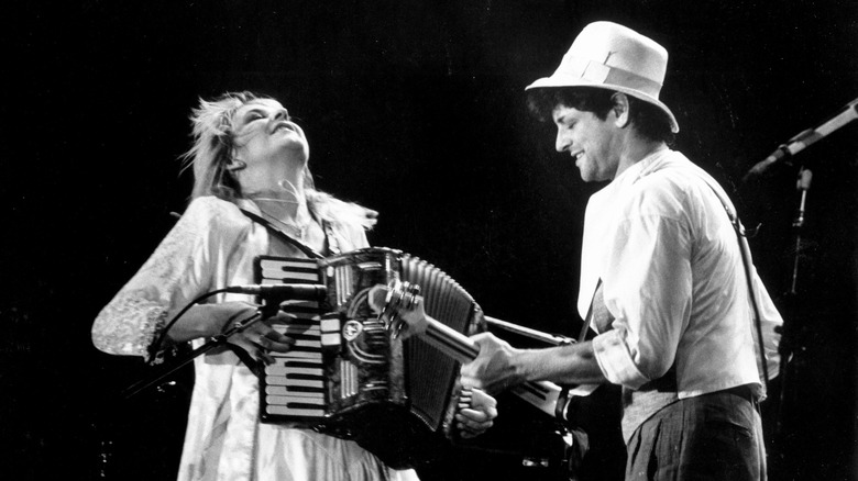 Stevie Nicks playing an accordion and Lindsey Buckingham playing a guitar onstage together.