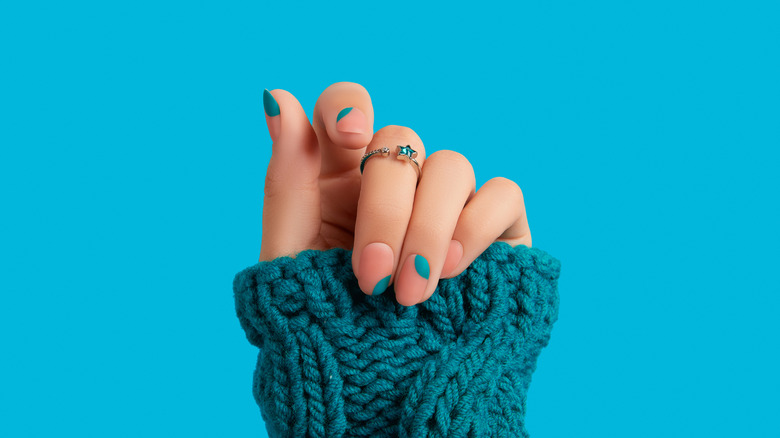 manicured hand in teal sweater
