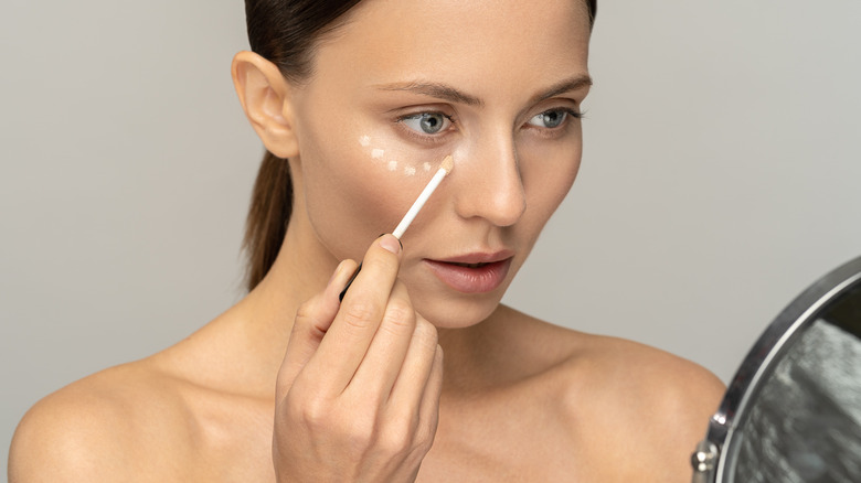 Woman applying concealer to under eyes 