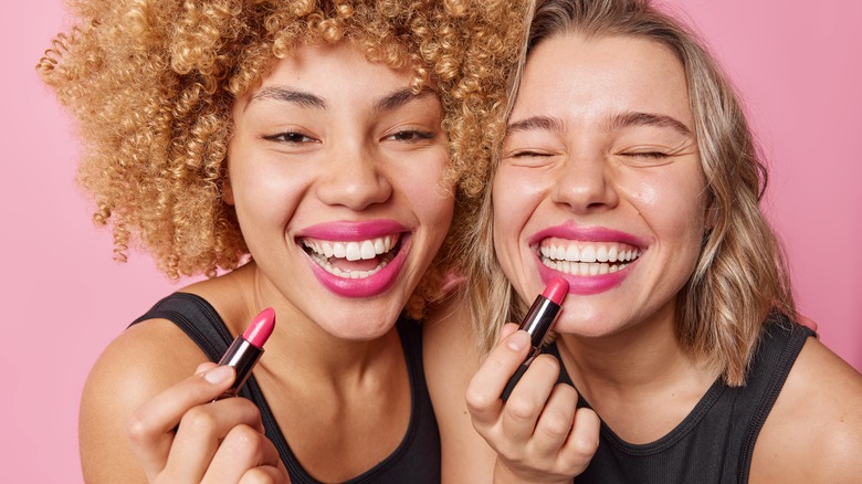 women smiling and applying lipstick