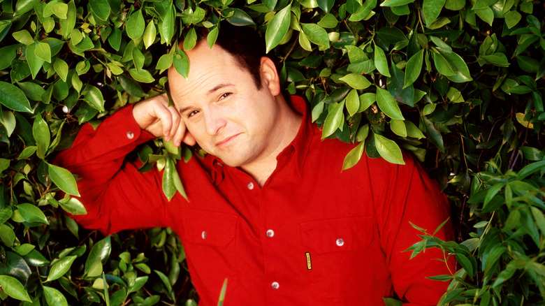 Jason Alexander (wearing a red shirt) posing for a promotional photo (in a bush) in 1990