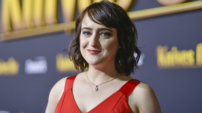 Mara Wilson posing at an event in a red dress and dark red lipstick
