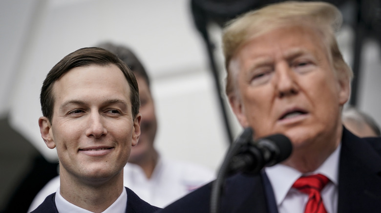 Jared Kushner smiling behind Donald Trump.