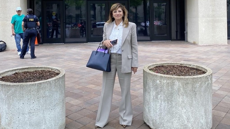 Maria Bartiromo standing in front of a stone building in a suit, two people stand behind her.