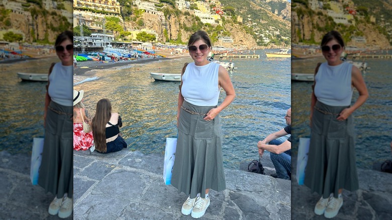 Maria Bartiromo in sunglasses standing in front of a beach with large mountains behind her.