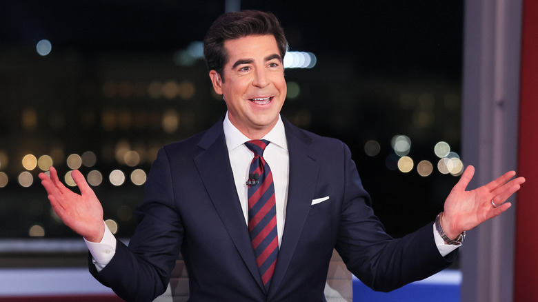 Jesse Watters raising his hands while speaking in a suit