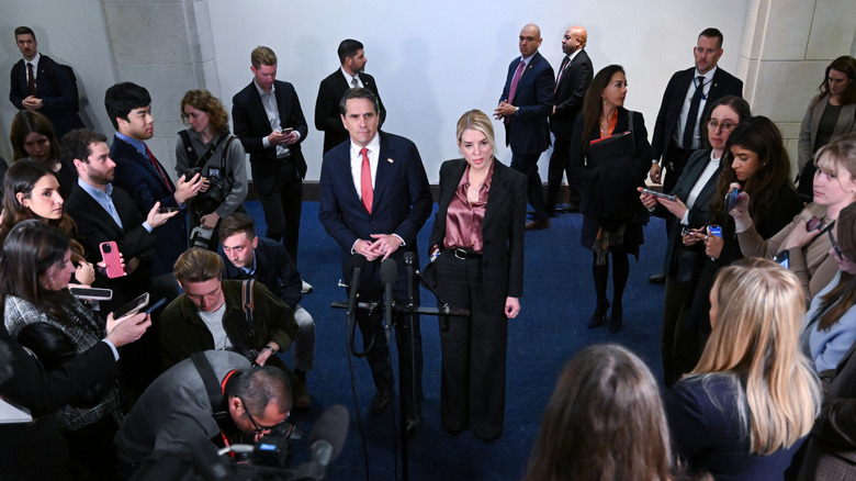 Pam Bondi and her replacement, Todd Blanche, surrounded by reporters from different media outlets